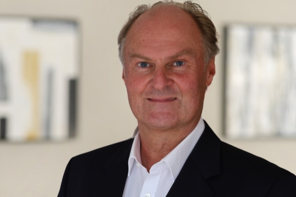 White man Peter Kindermann in a black suit and white open collared shirt